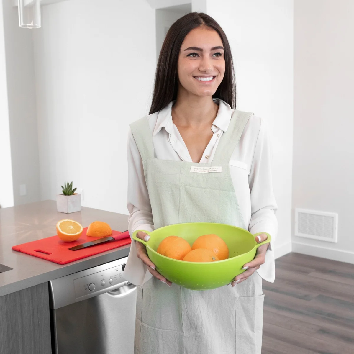 Wearing a light Hanee cotton cross-back apron while holding a bowl of oranges in the kitchen