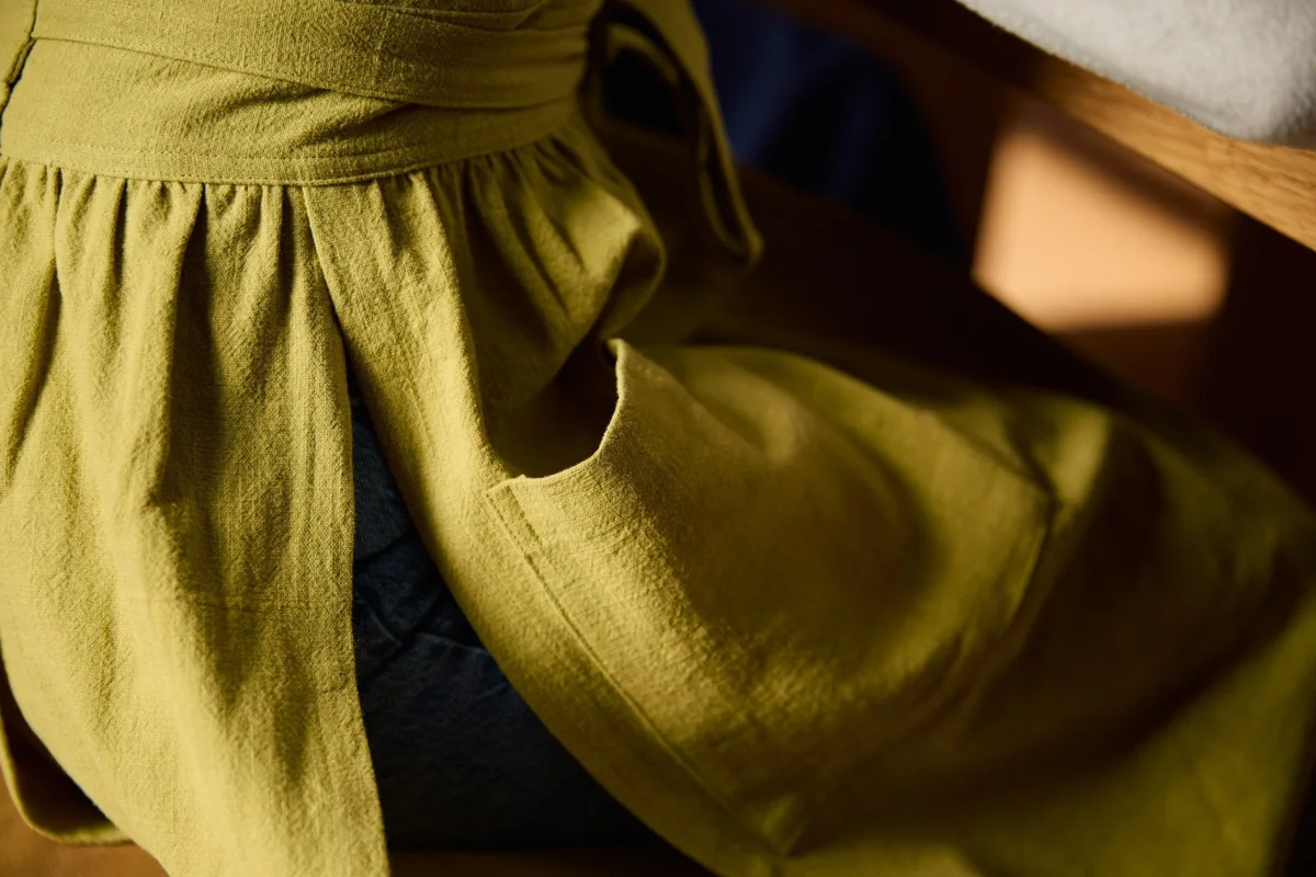 Close-up of a Hanee pinafore's gathered waist, stitching, and natural fabric